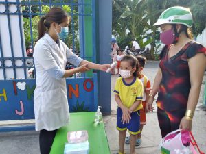 Nhân viên y tế trường học thực hiện đo thân nhiệt và cho trẻ rửa tay